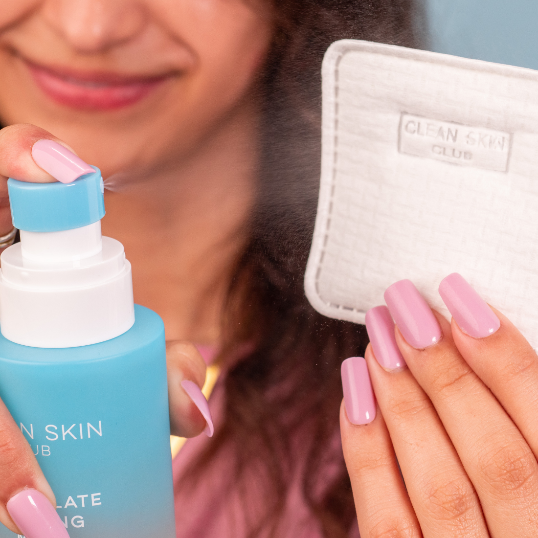 Person holding a blue skincare product and a white pouch with &