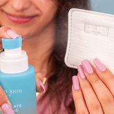 Person holding a blue skincare product and a white pouch with &